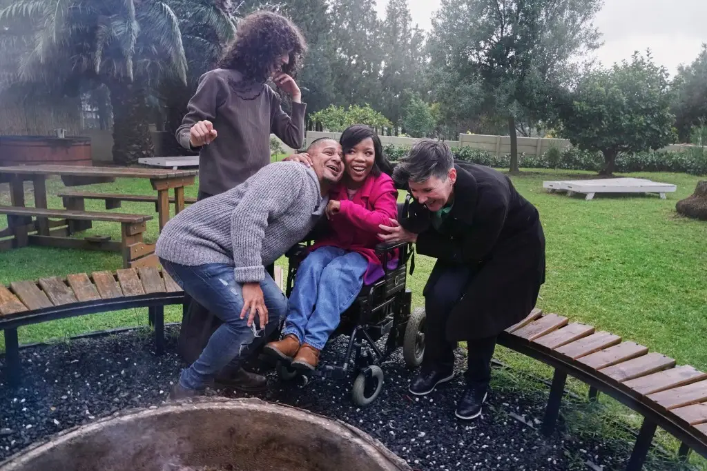 Group of friends, one in wheelchair, outside by bonfire smiling and hugging